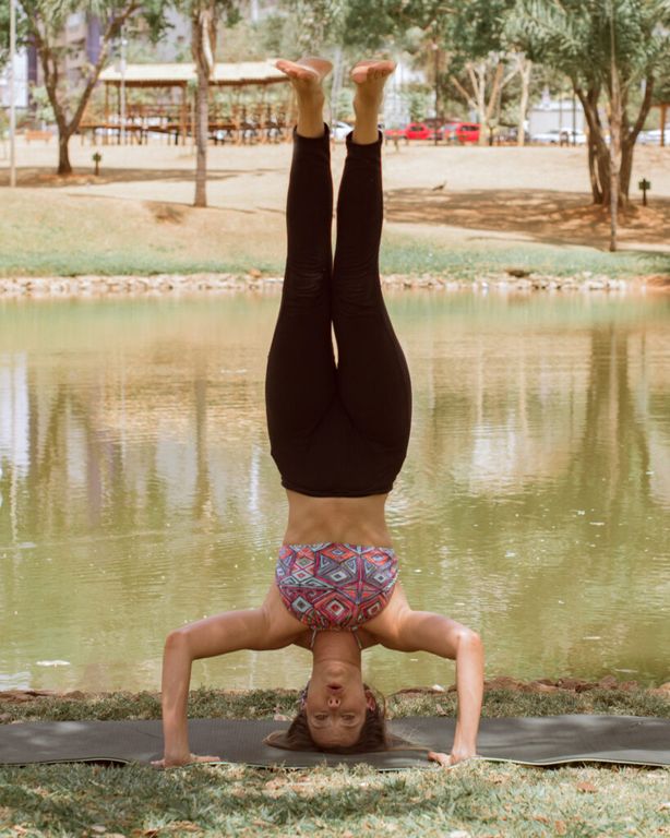 Mulher em um parque realizando uma postura invertida do yoga, de ponta cabeça.